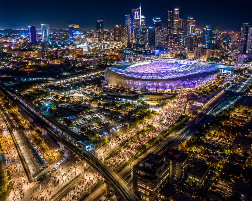 Best hotels for event travel — aerial view of a stadium at night with metro transit lines connecting venues to surrounding city neighborhoods