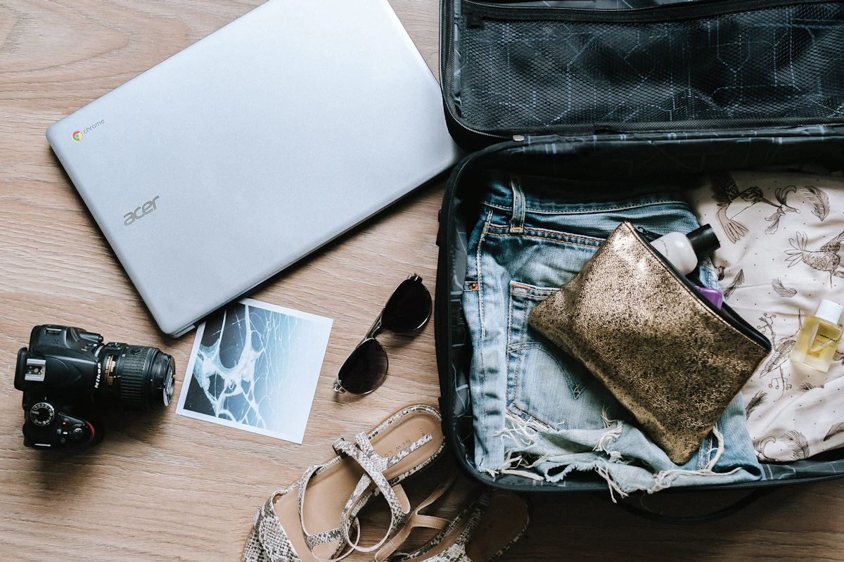 Open suitcase with clothing beside a laptop and camera