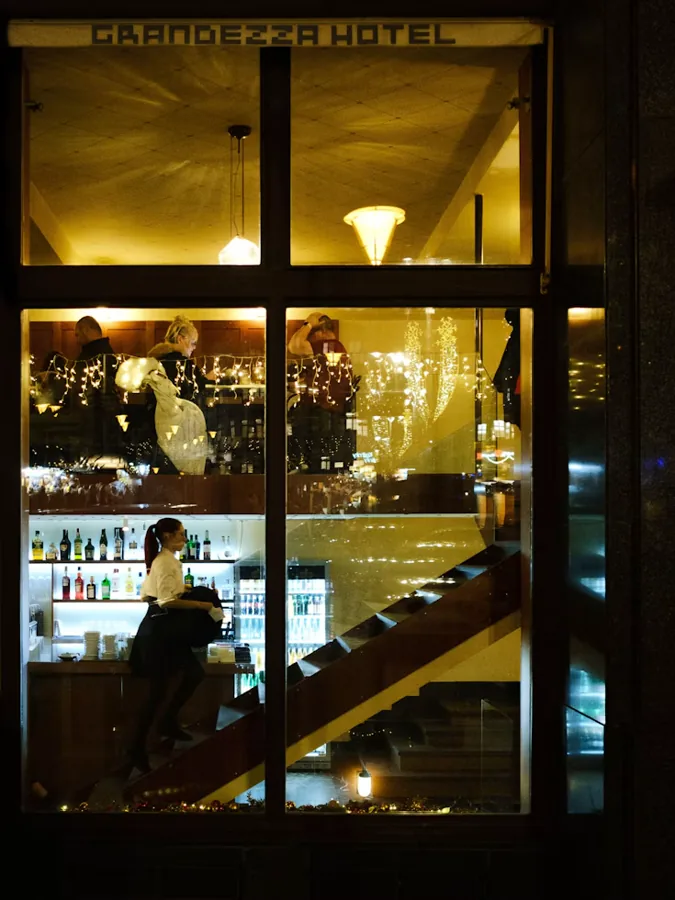 People inside a warmly lit hotel lobby and bar at night